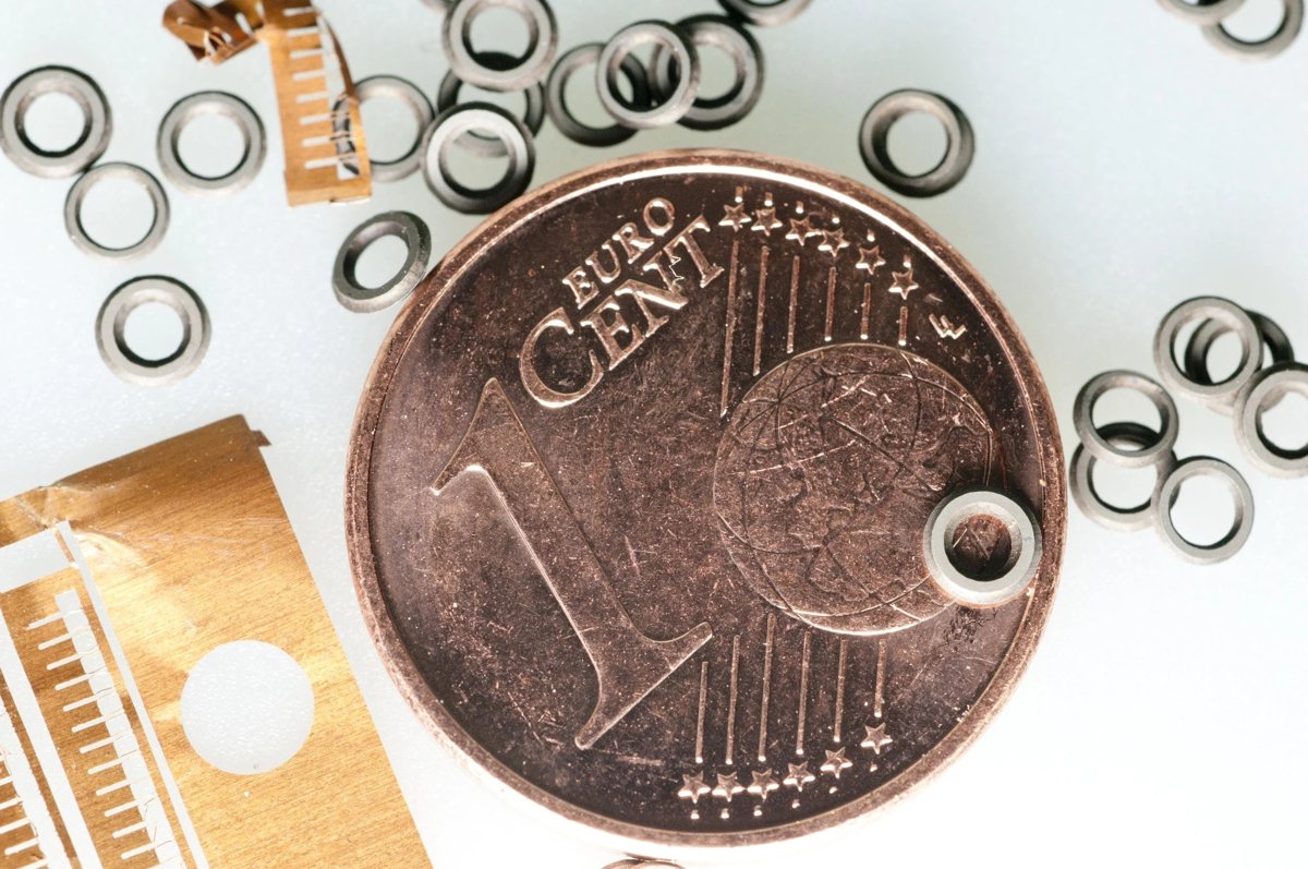 Winzige geätzte Metallringe und Kammstrukturen neben einer 1-Cent-Münze als Größenvergleich